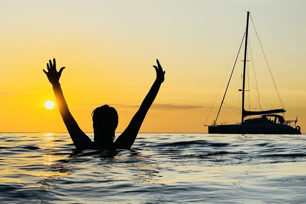 Life coach Katarina Stoltz in silhouette at in the sea in Thailand at sunset with her arms raised in celebration.