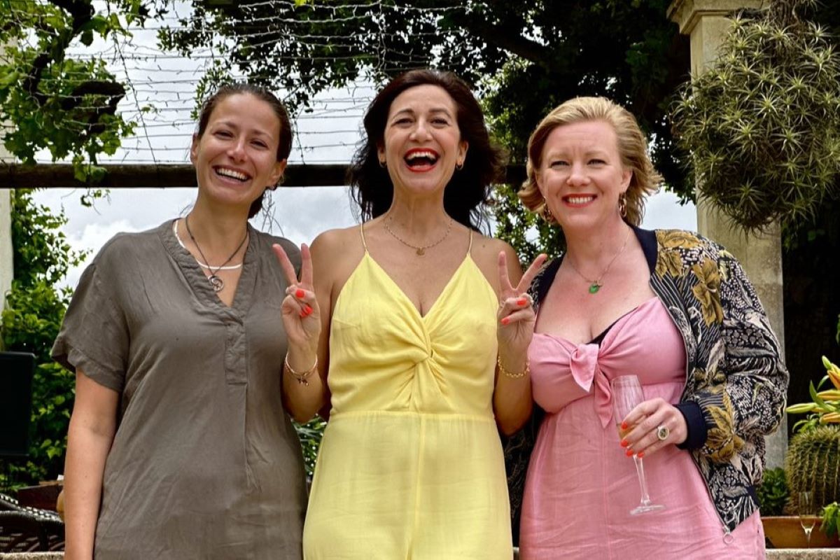 Life coach and therapist Katarina Stoltz smiling in a yellow jumpsuit with 2 female friends stood either side of her as they celebrate her birthday in Mallorca