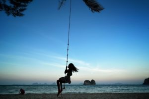 Silhouette of Life Coach Katarina's daughter on a rope swing on the beach in Thailand as the sunsets