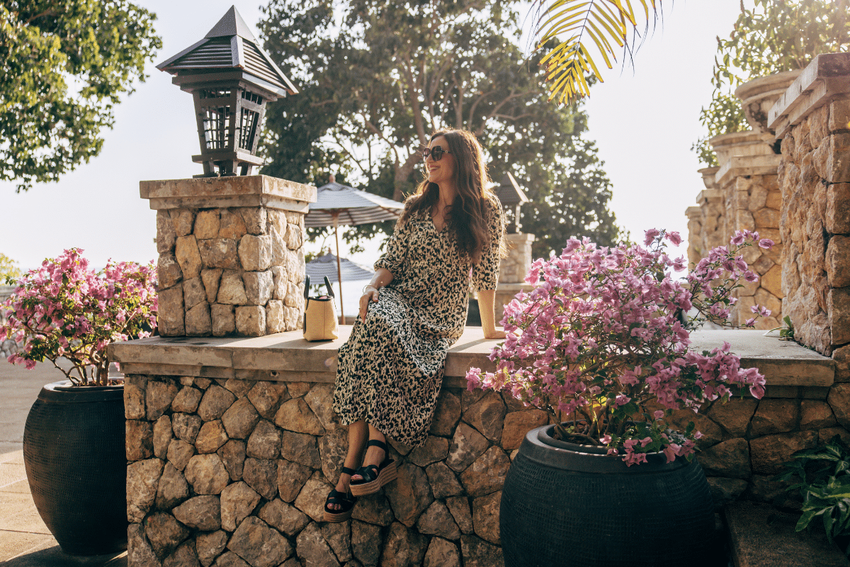 Life coach Katarina Stoltz sitting on a wall next surrounded by flowers contemplating fear, change and moving forward.