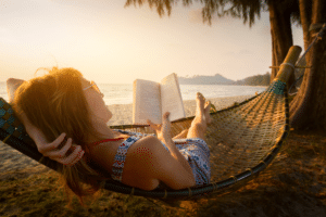 Young woman lying in a hammock reading a book on the beach