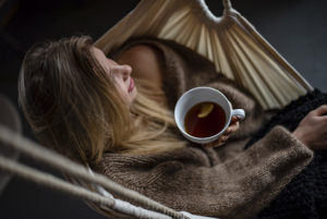 Woman resting in hammock with a hot drink.