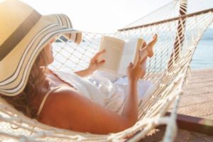 Woman reading in a hammock on a sunny beach and resting without guilt.